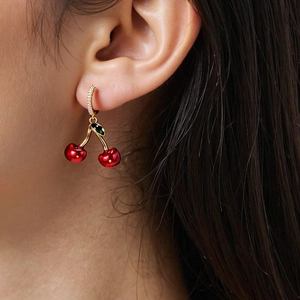 Close-up of red cherry drop earrings with green leaves and gold rhinestone hooks