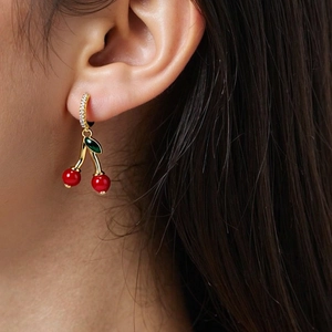 Close-up of red cherry earrings with gold diamond-set clips on woman wearing them