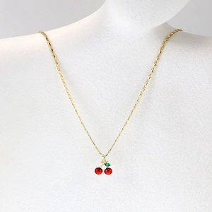Detailed close-up of red cherry pendant necklace with green leaf on a gold chain
