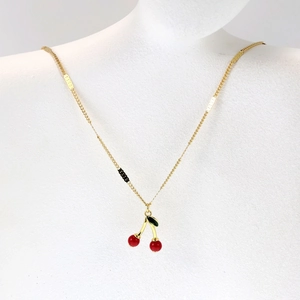 Close-up of golden cherry pendant necklace with red beads and green leaf on mannequin