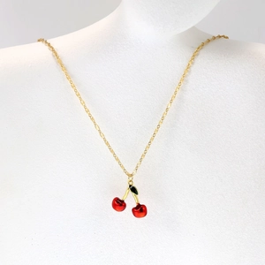 Detail of a gold-tone twisted chain necklace with red cherry pendants and green leaves