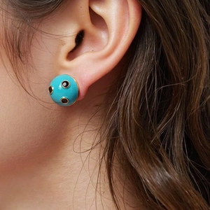 Close-up of model wearing a turquoise semicircular stud earring with black stone dots