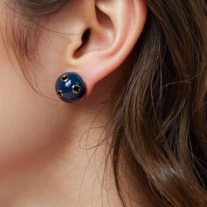 Detailed close-up of dark blue enamel dome earring with gold trim worn by a model