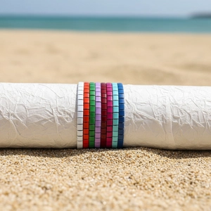 Nahaufnahme bunter Tila-Perlenarmbänder auf weißem Ständer vor einem Sandstrand