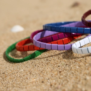 Bunte Tila-Perlenarmbänder gestapelt auf Strandsand im sommerlichen Boho-Stil