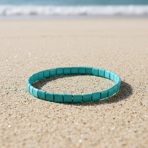 Türkisblaues Tila-Perlenarmband auf Sand mit Meereshintergrund im Boho-Strandstil