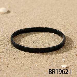 Detail eines minimalistischen schwarzen Tila-Perlenarmbands auf Sand mit Strandflair