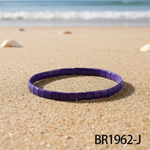 Detail eines dunkelvioletten Tila-Perlenarmbands am Strand mit Muscheln und Wellen