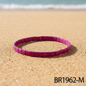 Nahaufnahme eines tiefvioletten Tila-Perlenarmbands auf Sand mit sanften Meereswellen