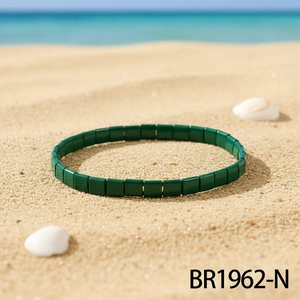 Detail eines dunkelgrünen Tila-Perlenarmbands auf Strandsand mit Muscheln und Meer