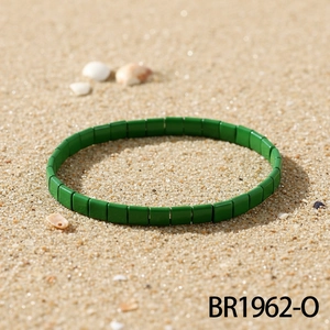 Detailaufnahme eines grünen Tila-Perlenarmbands auf sonnigem Sand mit Muscheldekor