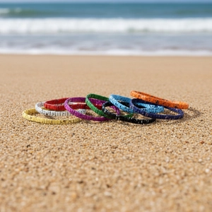 Detail of colorful woven cork bracelets stacked on a sandy beach under natural light