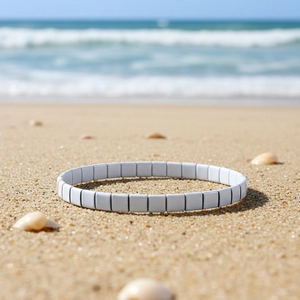 Nahaufnahme eines weißen Tila-Perlenarmbands auf Sandstrand mit sommerlichem Urlaubsgefühl