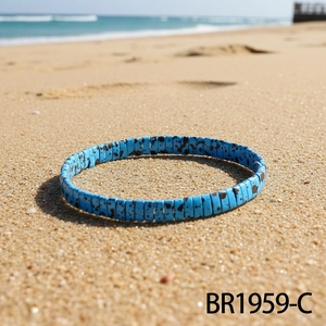 Detail of light blue beaded bracelet with brown spots resting on a sandy beach