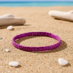 Detail of purple Tila bead bracelet with enamel finish on a sandy beach background