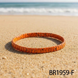 Close-up of orange tile-style handmade bracelet with black spots on a sunny beach