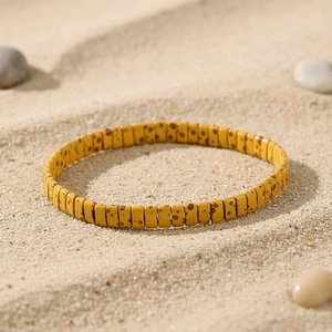 Detail of yellow tile beads with brown spots on a sandy beach background for bohemian style