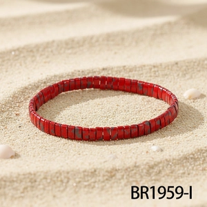 Detail view of red Tila beaded bracelet with marble texture on white sandy beach scenery