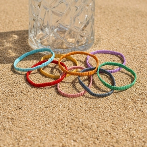 Détail de bracelets Tila en émail coloré sur le sable, bijoux de plage style bohème