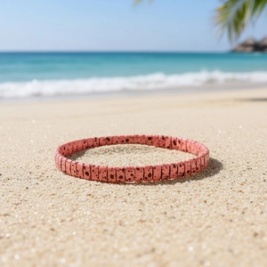 Detail of pink Tila bead bracelet with black spots on a sunny beach background