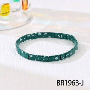 Detail of green Tila bead bracelet with white splatter dots on white textured fabric