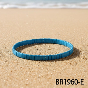 Bracelet en perles Tila bleu ciel sur le sable fin avec vagues d'océan au fond