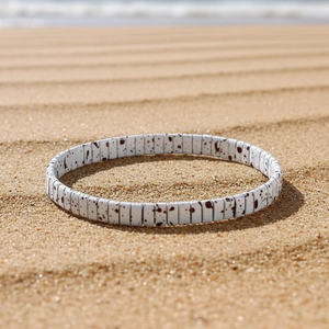 Close-up of white Tila bead bracelet with brown speckles on a summer beach background
