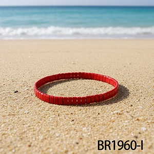 Gros plan d'un bracelet élastique en perles Tila rouges sur le sable de la plage