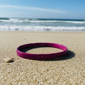 Détail d'un bracelet en perles Tila magenta sur le sable avec vue sur l'océan