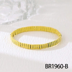 Gros plan d'un bracelet élastique en perles Tila jaune vif sur du papier blanc texturé