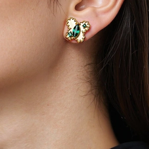 Golden butterfly stud earrings with sparkling green stones worn on a female ear