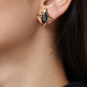 Macro detail of gold four-pointed star stud earring with marquise black zircon