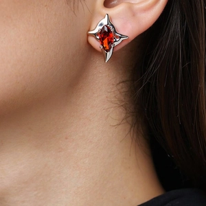 Detailed close-up of a silver four-pointed star earring with a vibrant red marquise zircon