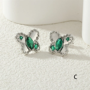 Detailed macro view of butterfly stud earrings with emerald green gemstones and silver base