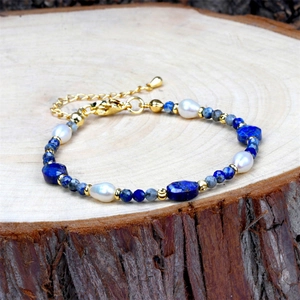 Detail van handgemaakte parelarmband met lapis lazuli en gouden sluiting op hout