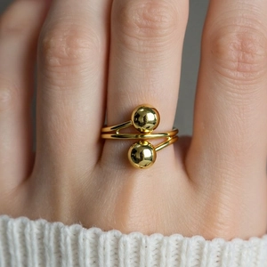 Close-up of a double-layer gold ball ring on finger with a soft knit sweater background