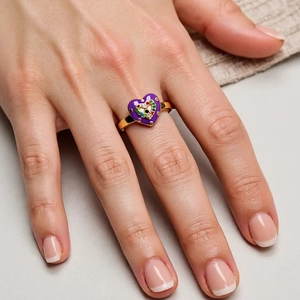 Close-up of golden open ring featuring purple heart enamel and evil eye charm on finger