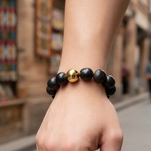 Bracelet en perles de bois noir mat avec perle dorée porté par un homme en extérieur