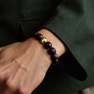 Gros plan d'un bracelet en perles de bois avec perle dorée polie sur un poignet d'homme