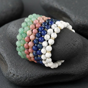 Detailed close-up of colorful gemstone beaded bracelets stacked neatly on natural stones.