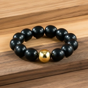Gros plan de perles en bois noir poli et d'une perle en métal doré brillant sur bois