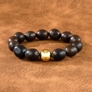 Détail macro du bracelet mala en bois brun foncé avec une perle d'espacement dorée