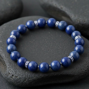 Close-up view of blue gemstone beaded bracelet with silver spacer beads on dark stone.