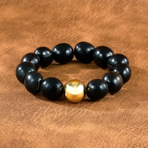 Gros plan d'un bracelet en bois avec une perle centrale dorée sur fond en cuir brun