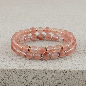 Close-up van dubbellaags roze edelsteen kraal armbanden met sprankelende metalen ringen.