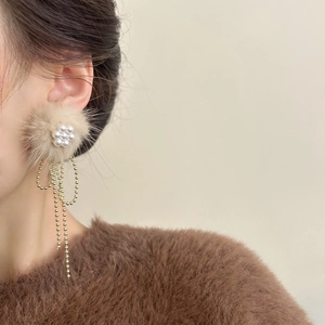 Winter style plush ball earrings with pearl flower and long golden tassel on a model