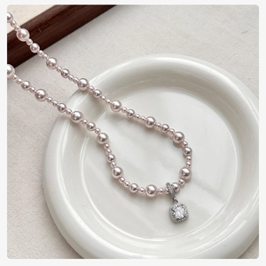 Macro detail of purple pearl necklace with square crystal pendant on white ceramic plate