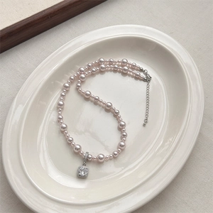 Pink pearl necklace with a square cubic zirconia pendant on a white ceramic plate