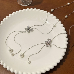 Elegante Halskette mit Schmetterlingsanhänger, Zirkonia und Perlen auf einem weißen Keramikteller