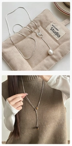 Dettaglio collana lariat argento con pietra occhio di tigre su borsa beige trapuntata